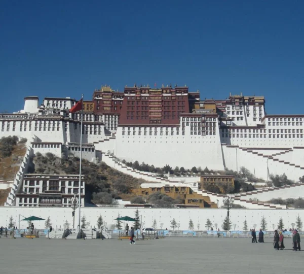 The grand Potala Palace in Lhasa, Tibet, featuring white and red stone architecture against a clear blue sky.