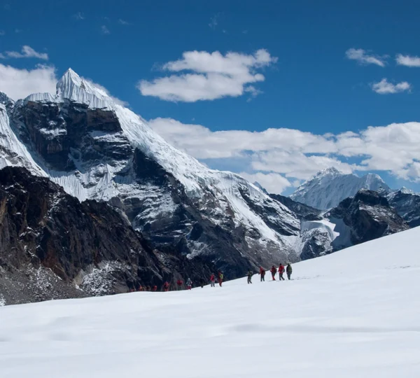 A group of tourists carefully crossing the snow-covered Cho-La Pass in the Everest region, navigating icy terrain at high altitude.