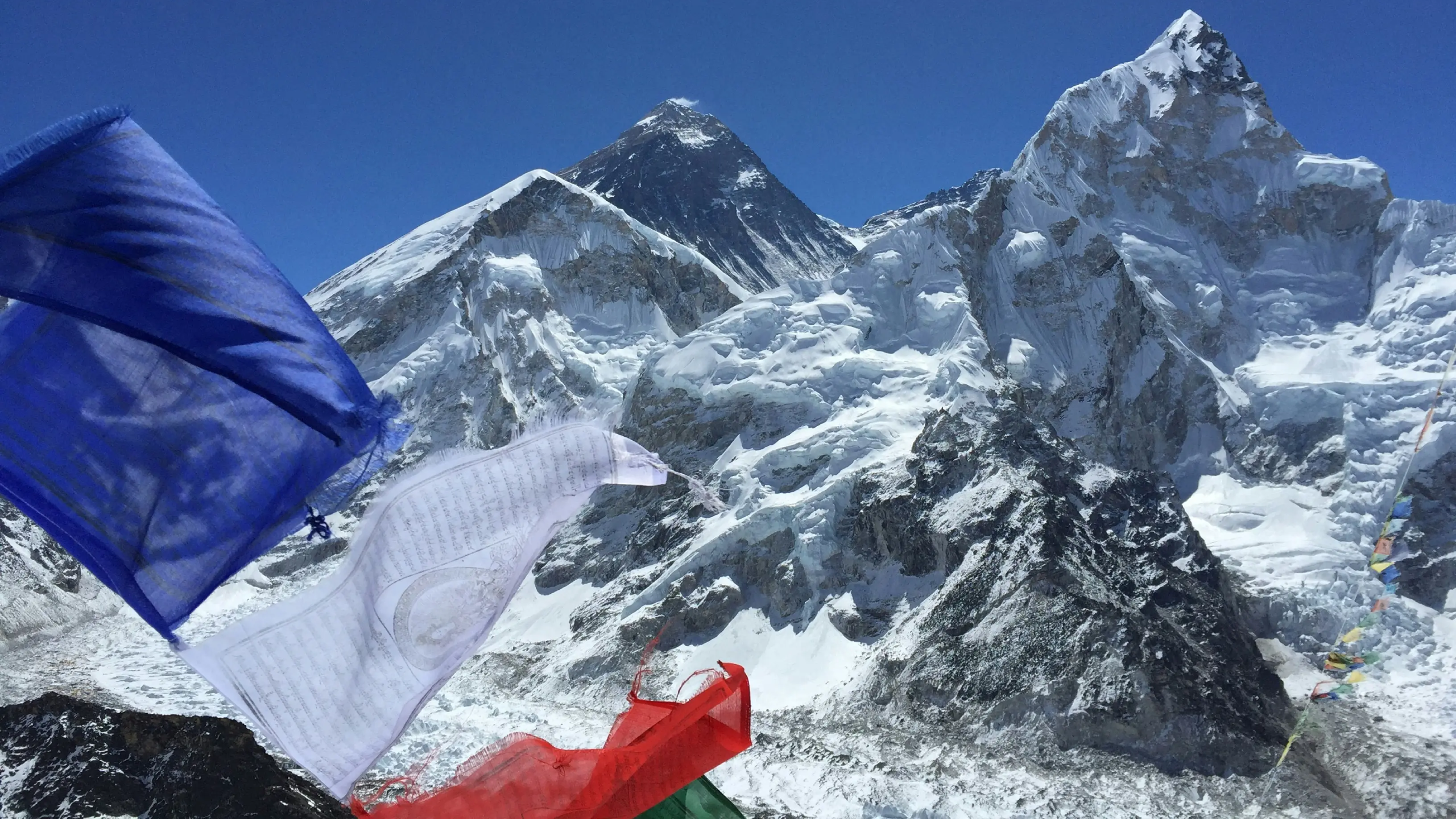 Colorful prayer flags at Everest Base Camp with snow-covered Himalayan peaks under a clear blue sky